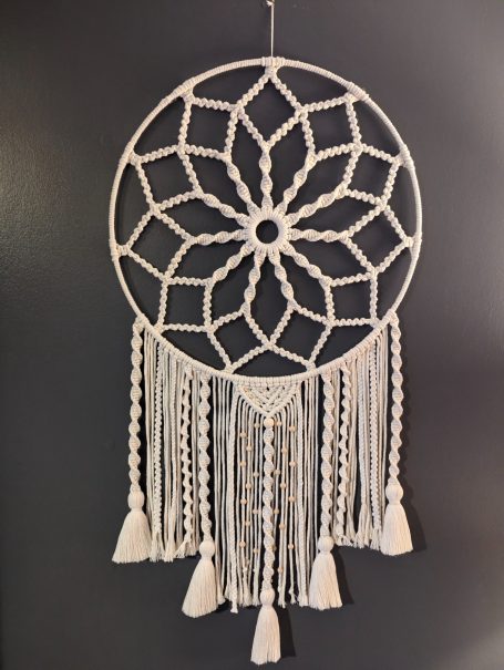 A decorative white dreamcatcher with a geometric pattern and flowing tassels.