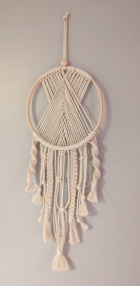 Macramé dreamcatcher with a circular frame and decorative tassels hanging down.