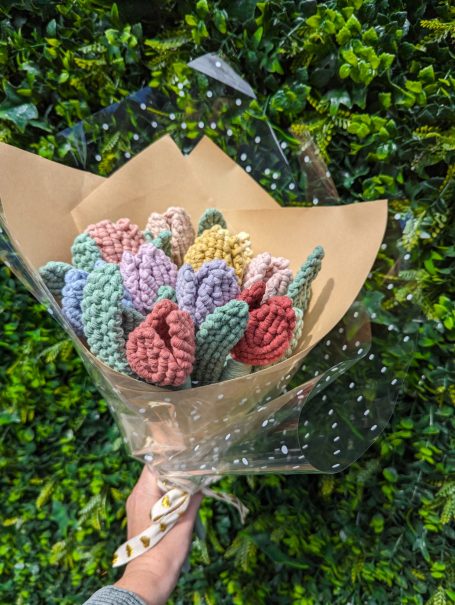A bouquet of colourful, textured tulips wrapped in kraft paper against a green backdrop.