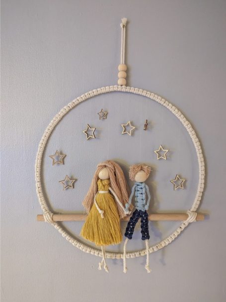 Two handcrafted dolls, a girl in a yellow dress and a boy in a blue shirt, on a hoop with stars.