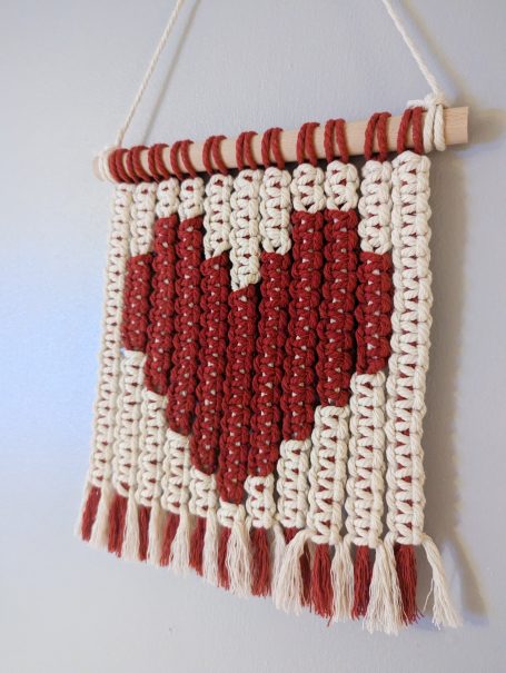 Woven wall hanging featuring a red heart on a cream background.