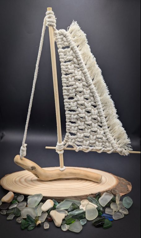 Model sailboat made from driftwood and macramé netting, surrounded by colourful sea glass.