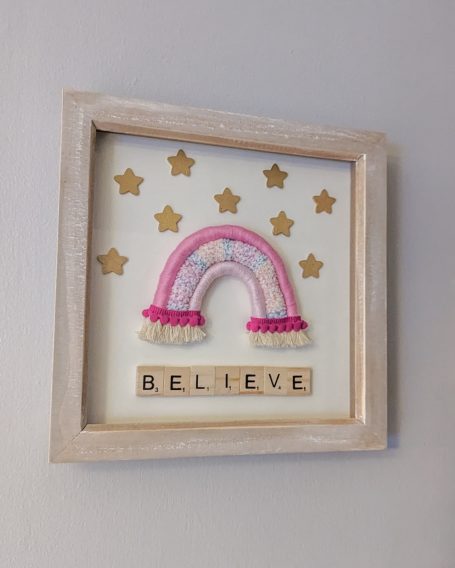Framed artwork featuring a rainbow and the word "BELIEVE" among gold stars.