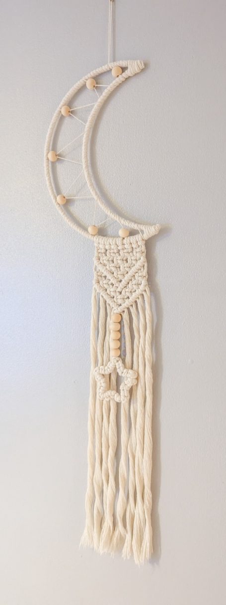 Macramé wall hanging in the shape of a crescent moon with a star detail.
