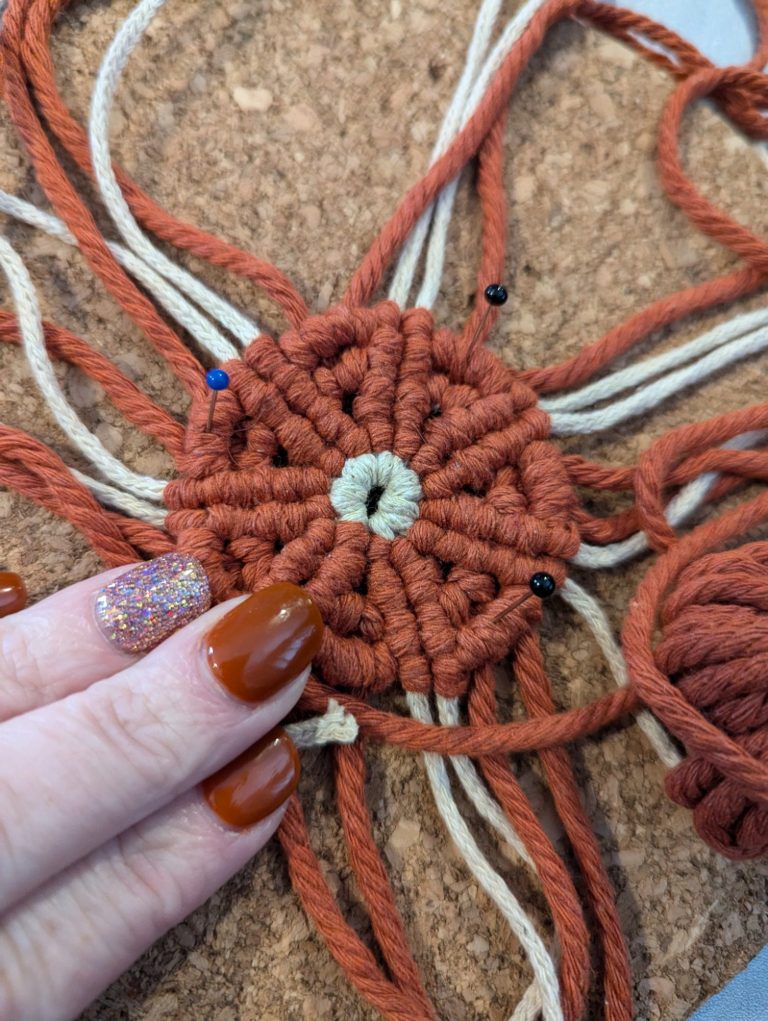 Hand with orange nails holding a macramé centrepiece made of braided rope.