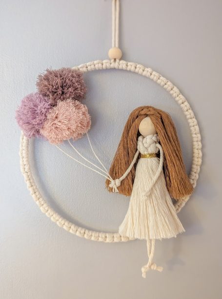 A decorative doll with brown hair, holding pastel pom-poms as balloons.
