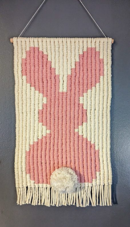 Woven wall hanging featuring a large pink bunny silhouette with a white pom-pom.