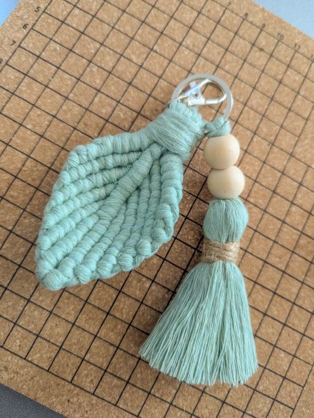 A mint green macramé keychain with wooden beads and a tassel.