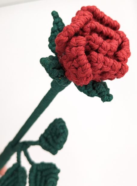 Handcrafted red macramé rose with green leaves and stem.