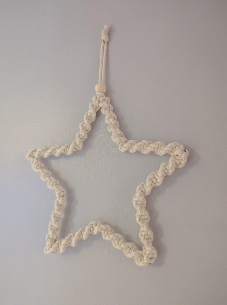 White rope star hanging on a light grey wall.