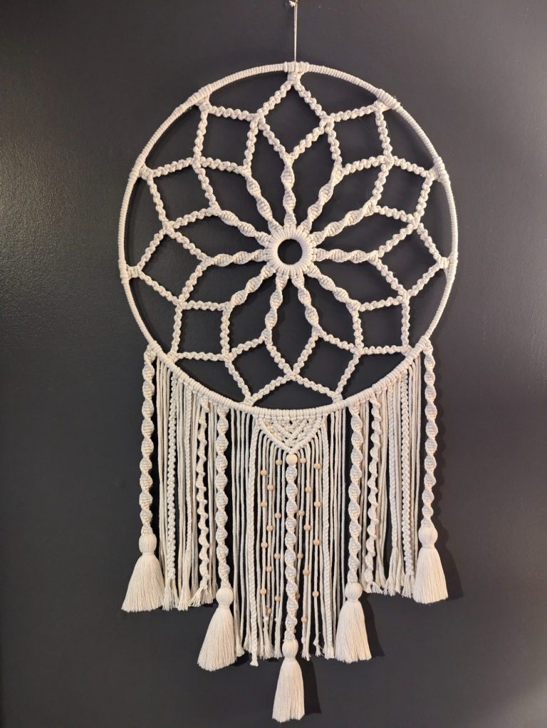 A white macramé dreamcatcher with a floral design and hanging tassels.