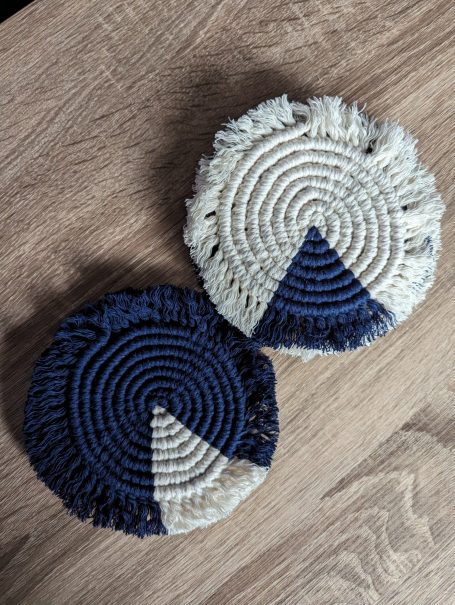 Two circular coasters with a navy blue and cream pattern, featuring fringed edges.